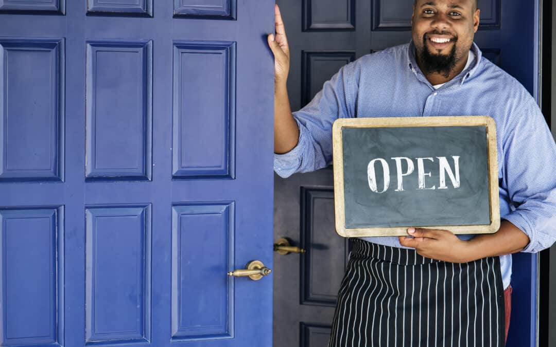 Entrepreneur man holding an open sign while holding a blue door. This is to represent that we are open in July