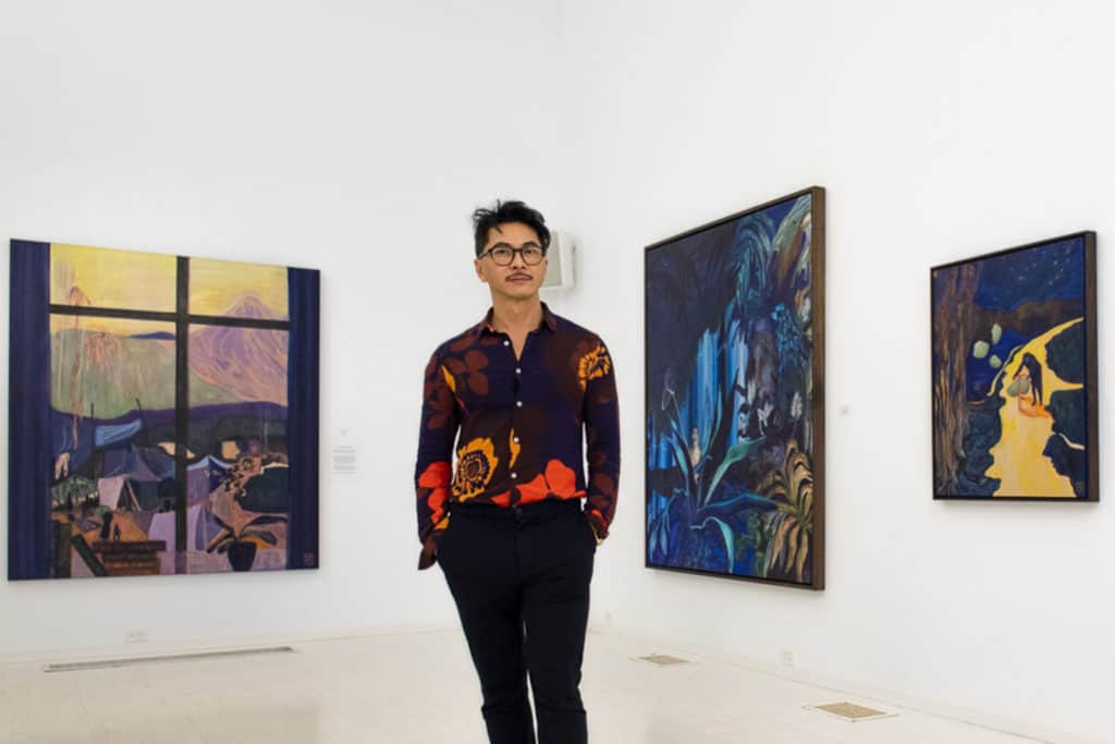 December January Client of the Month Tuan Vu stands in a gallery  with his paintings behind him